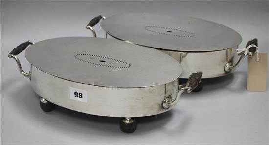 A pair of plated oval dish warmers, on ebonised bun feet